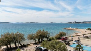 A coastal view with a clear sky, trees, parked cars, and a beach. - Apartments Ivan by the sea (Vodice)