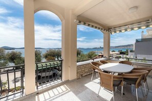 Un balcon avec une table et des chaises, donnant sur une étendue d’eau et sur une terre lointaine.