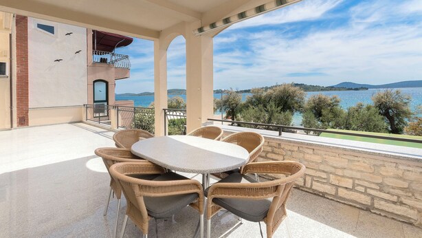A balcony with wicker furniture, a view of the sea, and a stone wall. - Apartments Ivan by the sea (Vodice)