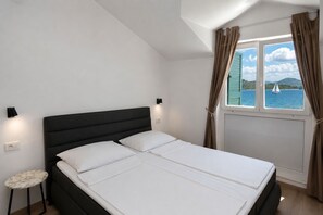 Une chambre à coucher avec un lit, une petite table, une fenêtre avec des rideaux et une vue sur la mer.