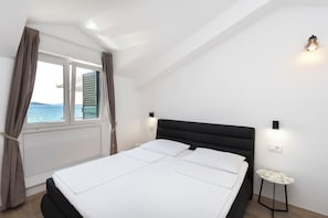 A bedroom with a bed, a window with curtains, a nightstand, and a wall-mounted light. - Apartments Ivan by the sea (Vodice)