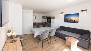 A modern living space with a dining table, gray sofa, and a kitchen area. - Apartments Ivan by the sea (Vodice)