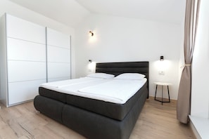 Egy modern hálószoba, amelyben egy nagy ágy, egy szekrény, éjjézőlámpák és egy kis asztal található.