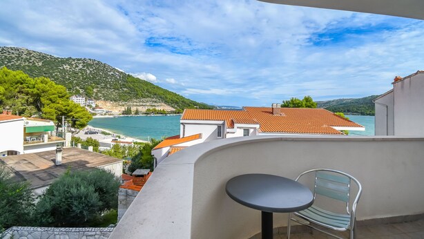 Ein Balkon mit Tisch und Stuhl mit Blick auf eine Küstenstadt, Gebäude und einen Berg.