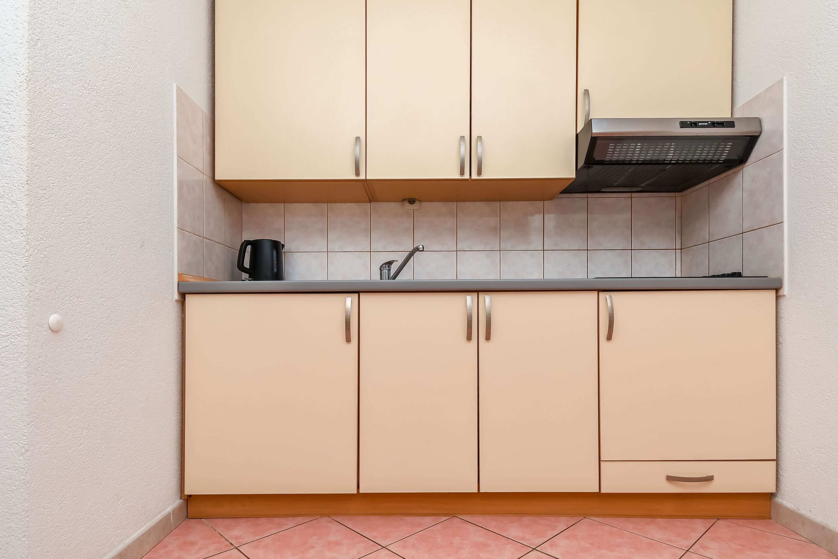 A kitchen with beige cabinets, a stainless steel range hood, and a coffee maker on the countertop.