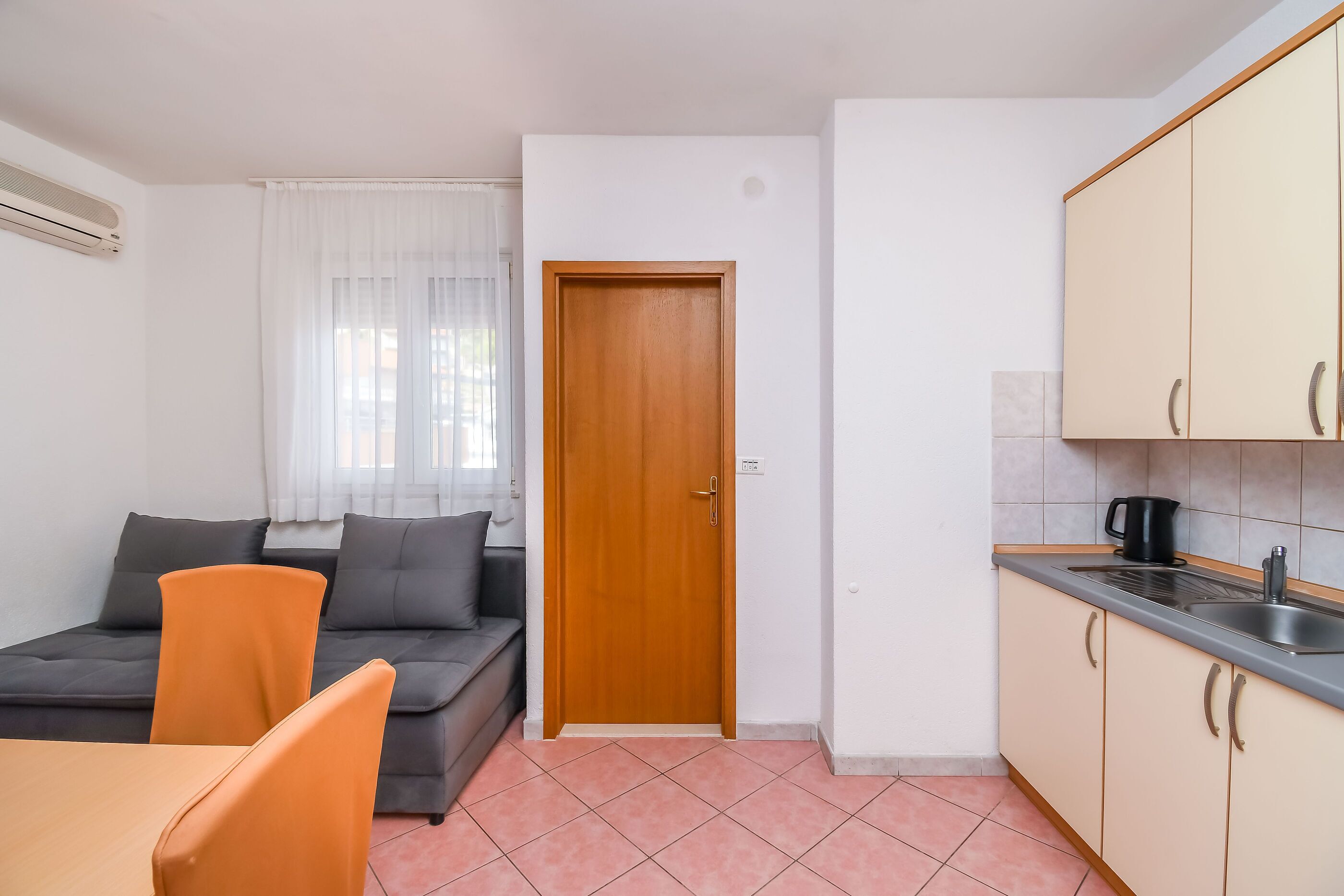 A compact living space with a sofa, a dining table with chairs, a kitchenette, and a wooden door.