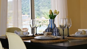 A dining table set with plates, cutlery, and wine glasses, with a vase of tulips and a view of a mountainous landscape through large windows. - Apartment Natasa (Vinisce)