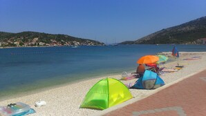 A beach with a row of colorful umbrellas and a green tent on the pebbled shore. - Apartment Natasa (Vinisce)