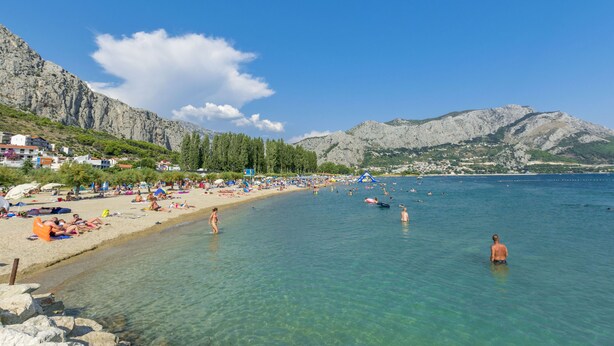 A beach with clear water, people swimming, and mountains in the background.