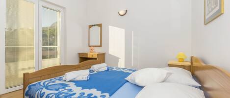 Een slaapkamer met een bed, een nachtkastje, een lamp, een spiegel en een raam met zonwering.