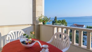 A balcony with a table set for tea, a bowl of fruit, and a potted plant.