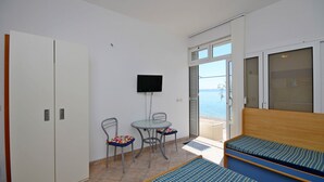 Una habitación con cama, televisión, mesa y sillas, y vista al mar.