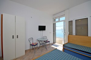 A room with a bed, a TV, a table with chairs, and a view of the sea. - Apartments Jure (Podgora)