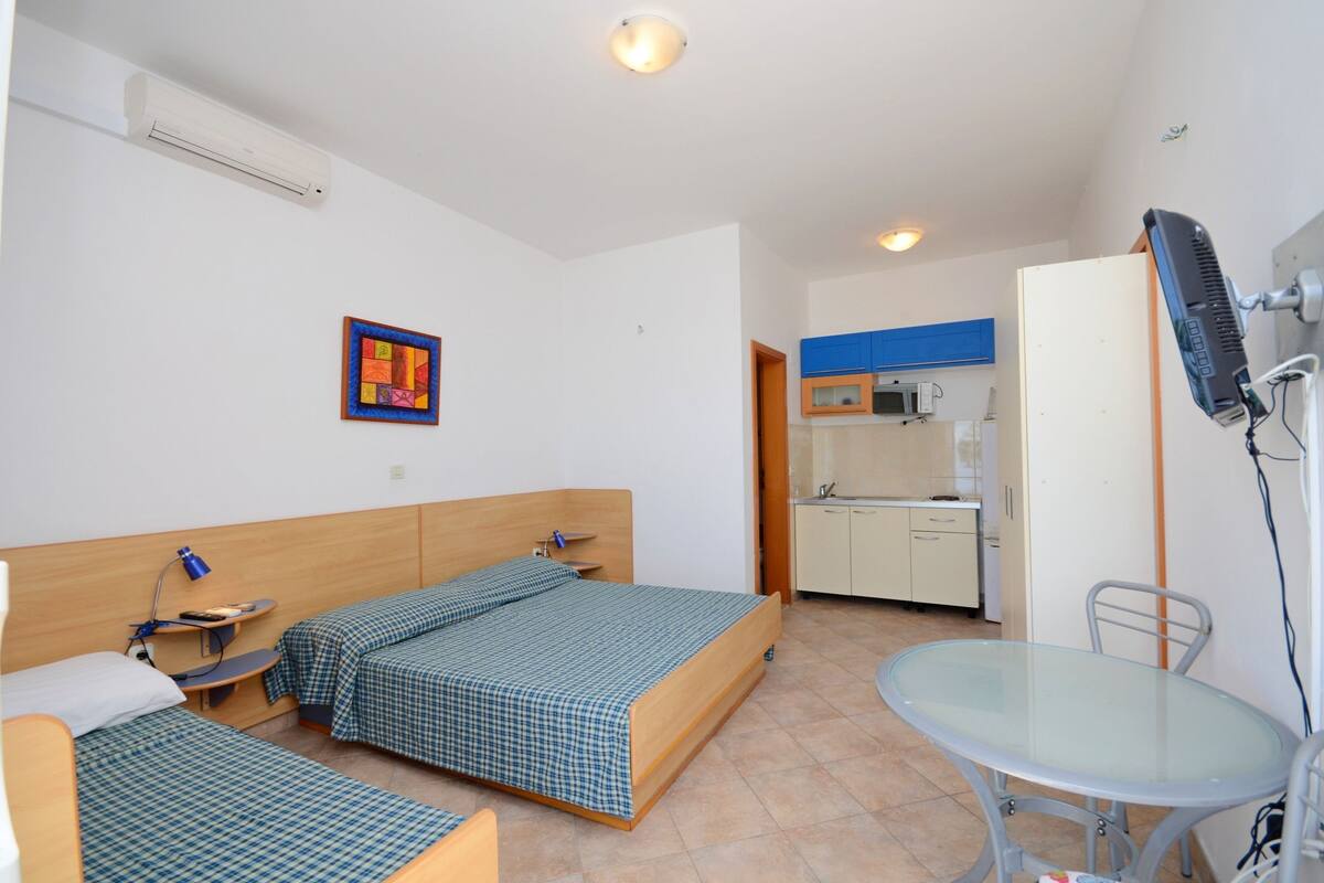 A hotel room with two beds, a small kitchenette, a glass table, and a ceiling fan.