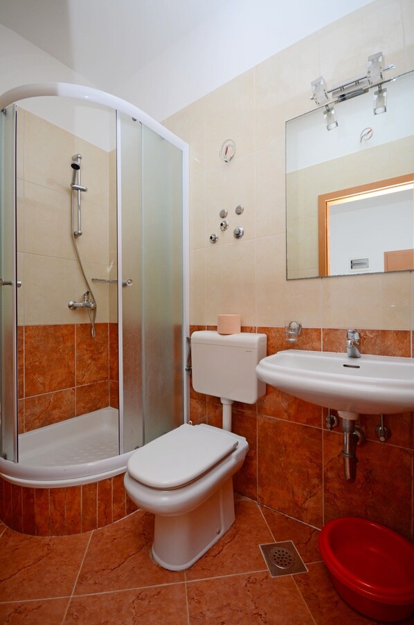 A bathroom with a glass-enclosed shower, a toilet, a sink, and a red basin.