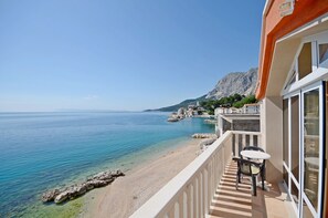 Un balcón con vistas al mar, una costa rocosa y una montaña en la lejanía.