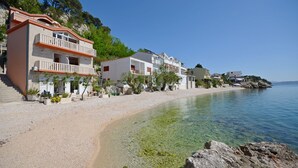 Un edificio costero con balcón, una playa despejada y agua tranquila.