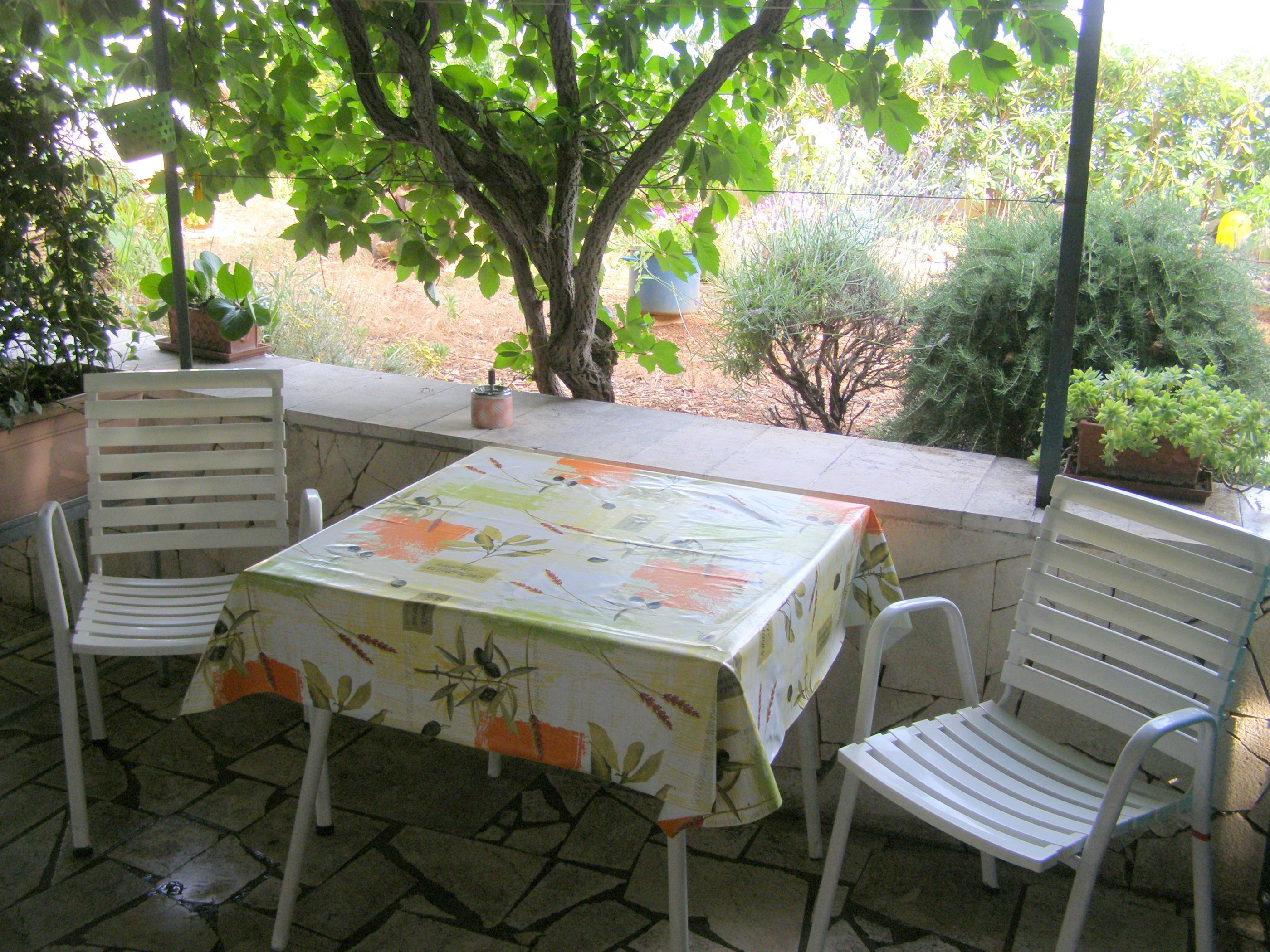 An outdoor patio with a table covered by a floral tablecloth, surrounded by white chairs.