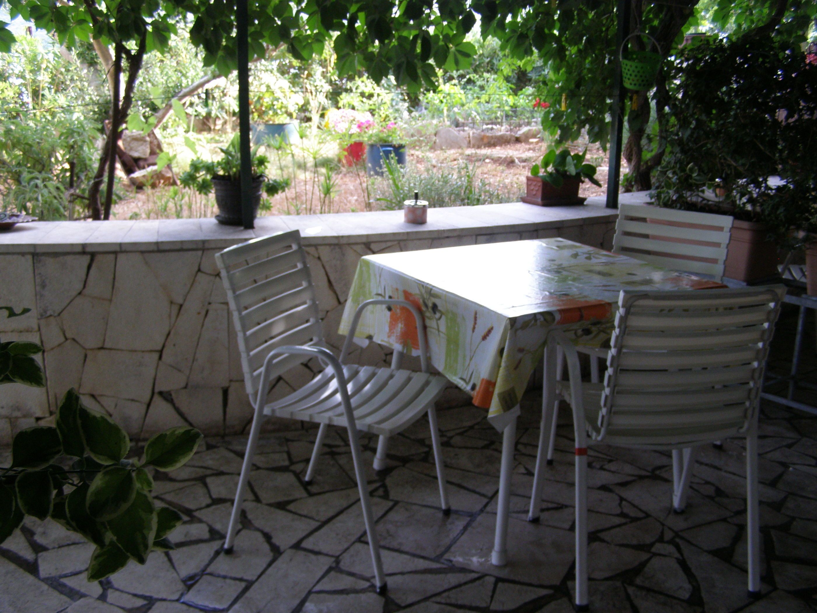 Un patio al aire libre con un muro de piedra, dos sillas de metal y una mesa cubierta con un mantel estampado.