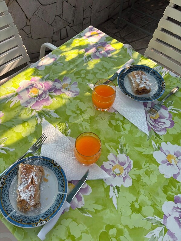 A table with a floral tablecloth, two plates with food, and two glasses of orange juice. - Apartment Zeljka (Seget Vranjica)