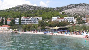 A beach with clear waters, umbrellas, and people. - Apartment Zeljka (Seget Vranjica)
