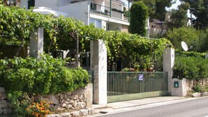 A two-story building with a balcony, surrounded by greenery and a stone wall. - Apartment Zeljka (Seget Vranjica)