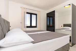 Ein modernes Schlafzimmer mit zwei Betten, einem großen Fenster und einem Spiegel.