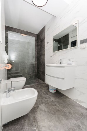 Ein modernes Badezimmer mit einer gläsernen Dusche, einem weißen Waschbecken mit Marmorplatte und einem großen Spiegel darüber.