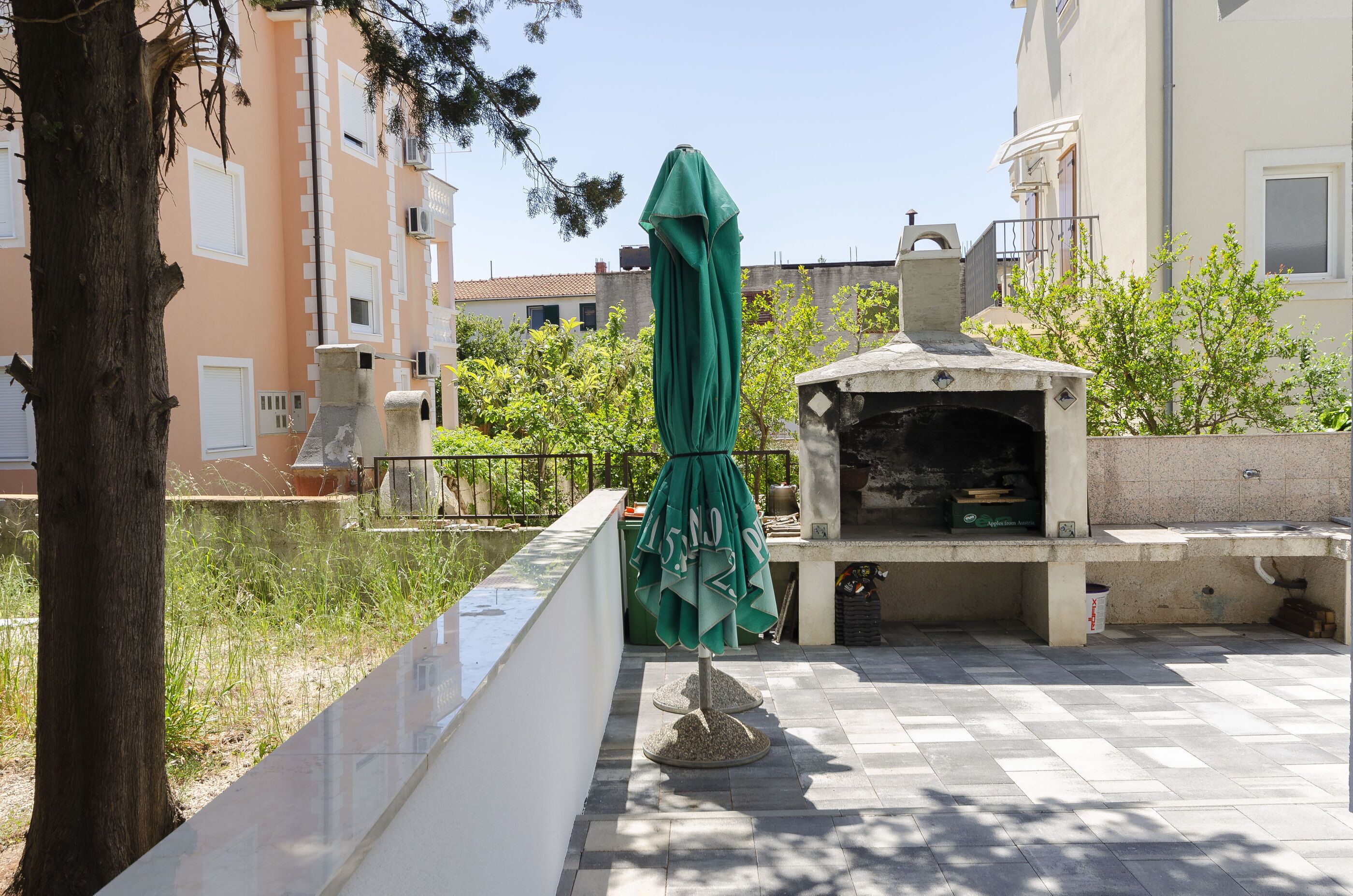 Ein Patio mit Sonnenschirm, Grill und Stehbank.