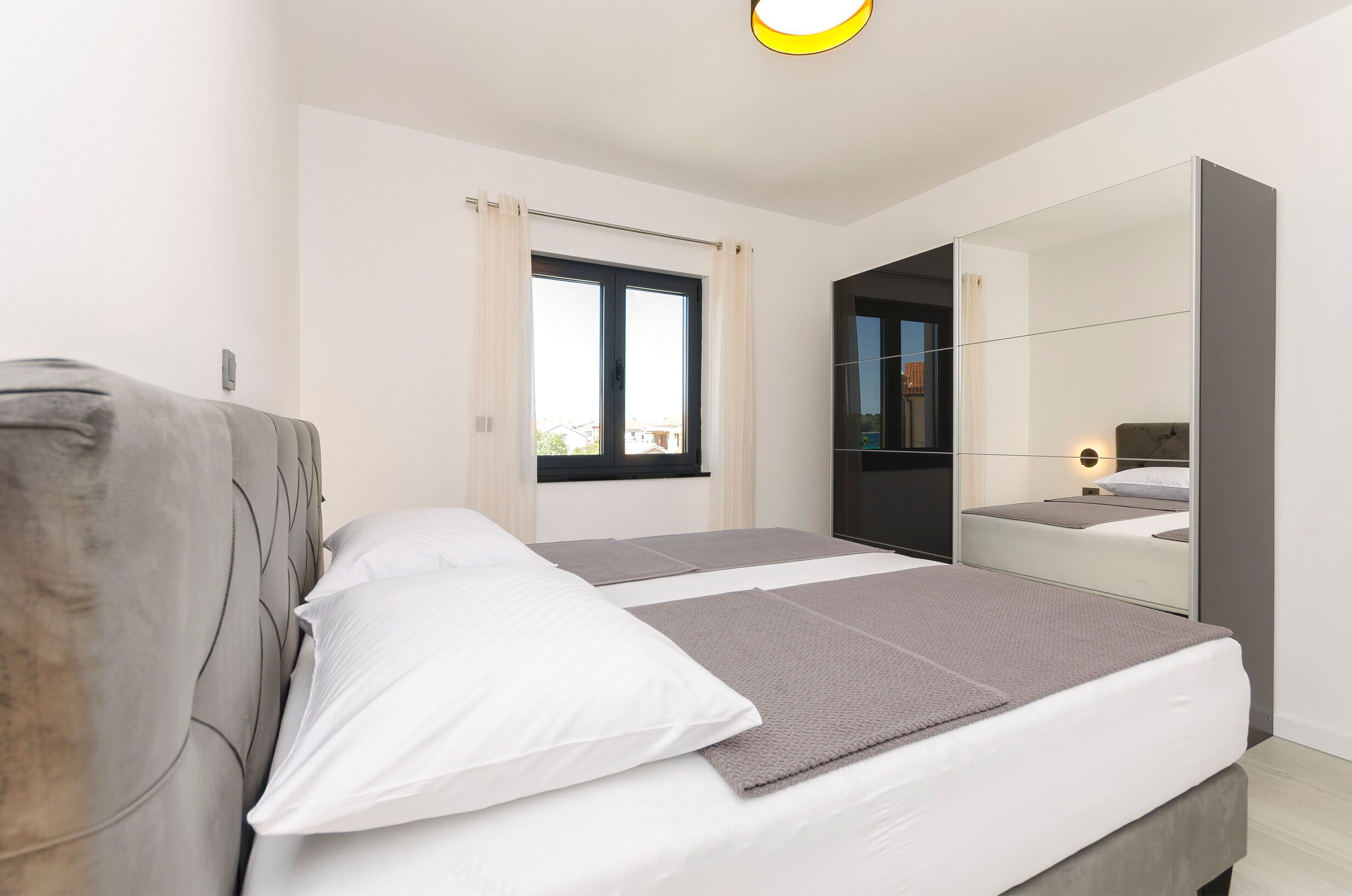 A modern bedroom with a bed, a large mirror, and a window with curtains.