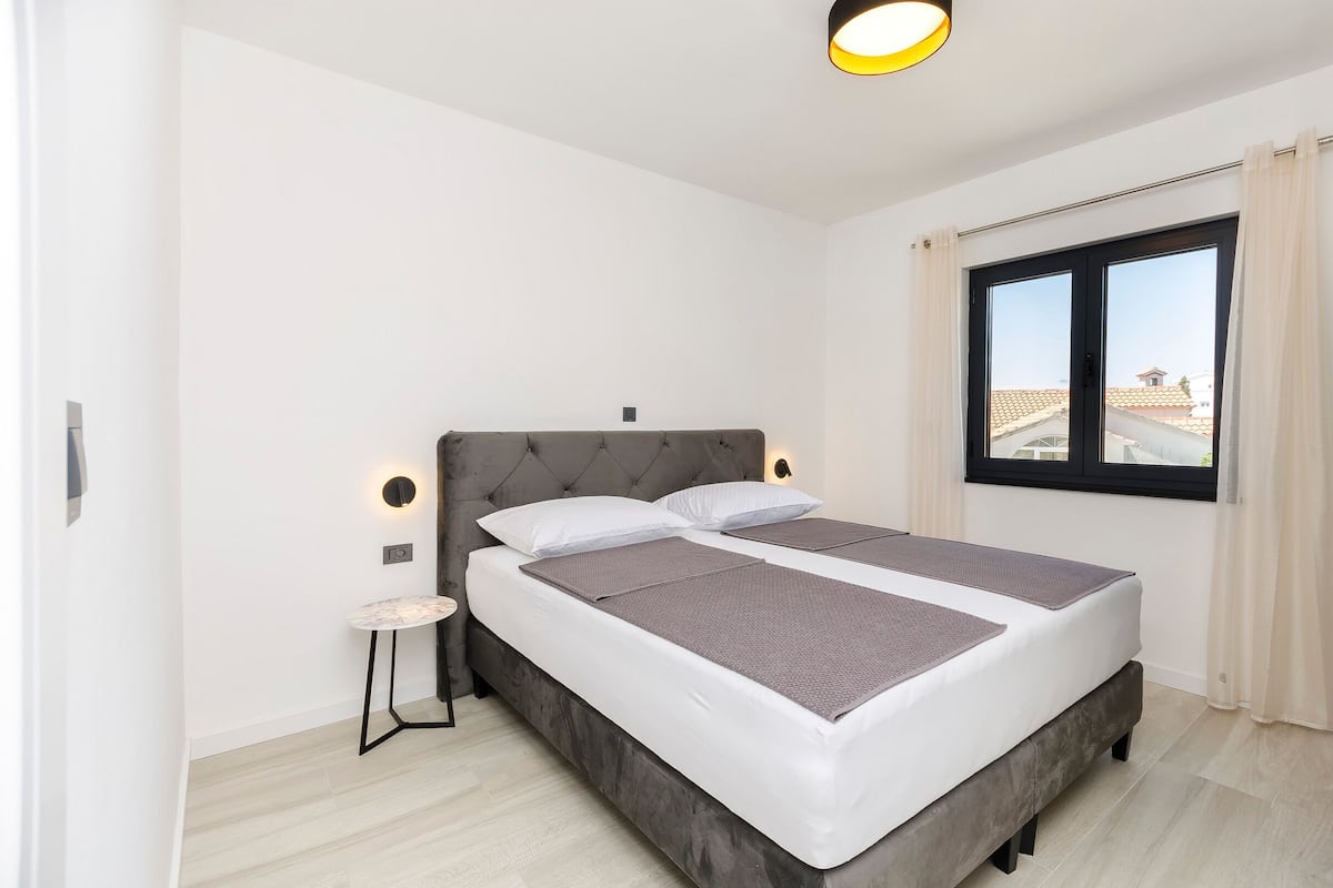Un dormitorio moderno con una cama grande, una mesita de noche y un ventanal con cortinas.