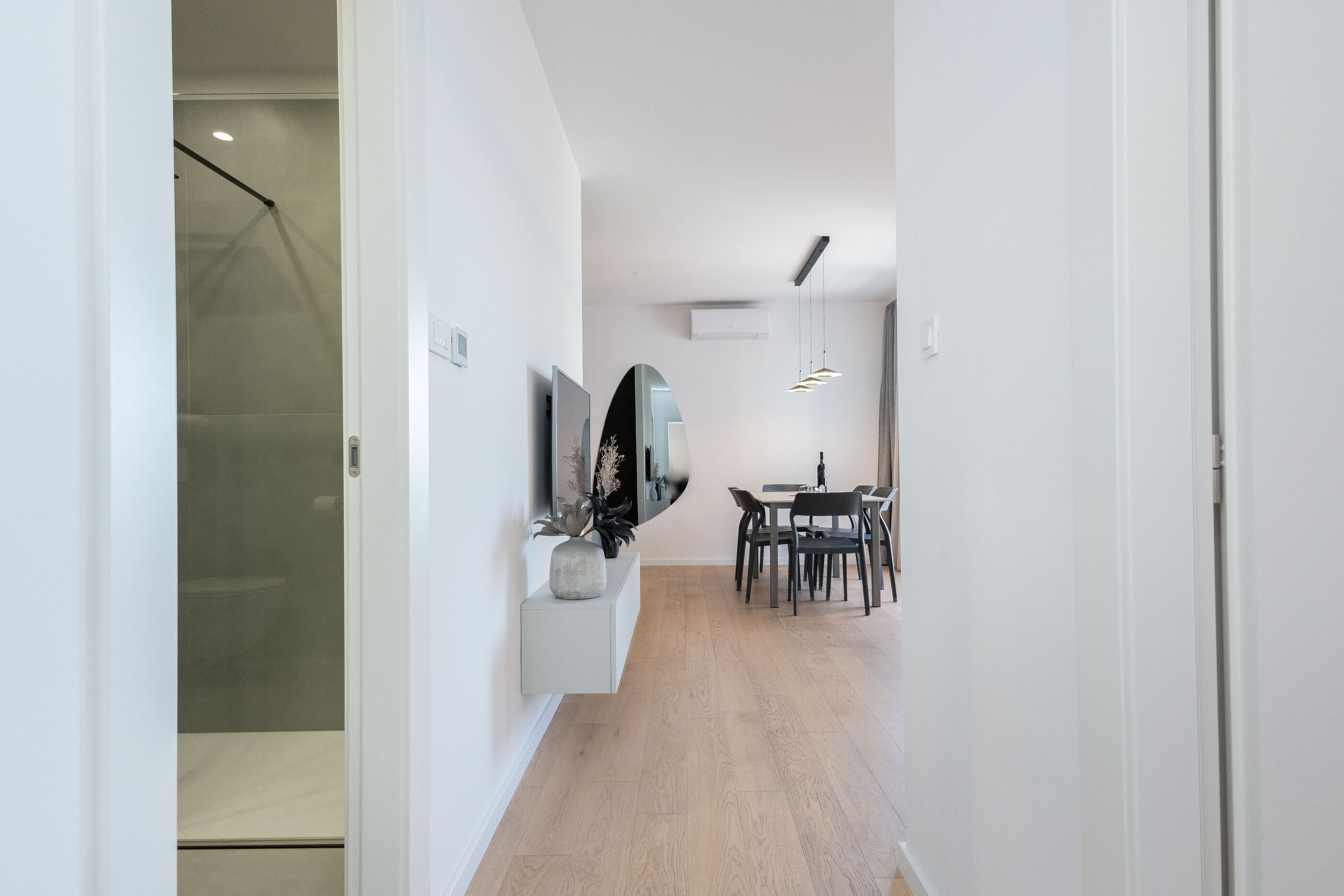 Un intérieur moderne avec un couloir menant à une salle à manger, un téléviseur fixé au mur et une douche visible.