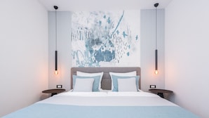 Una habitación de hotel moderna con una cama grande, dos mesitas de noche, una obra de arte en la pared y una lámpara del techo.