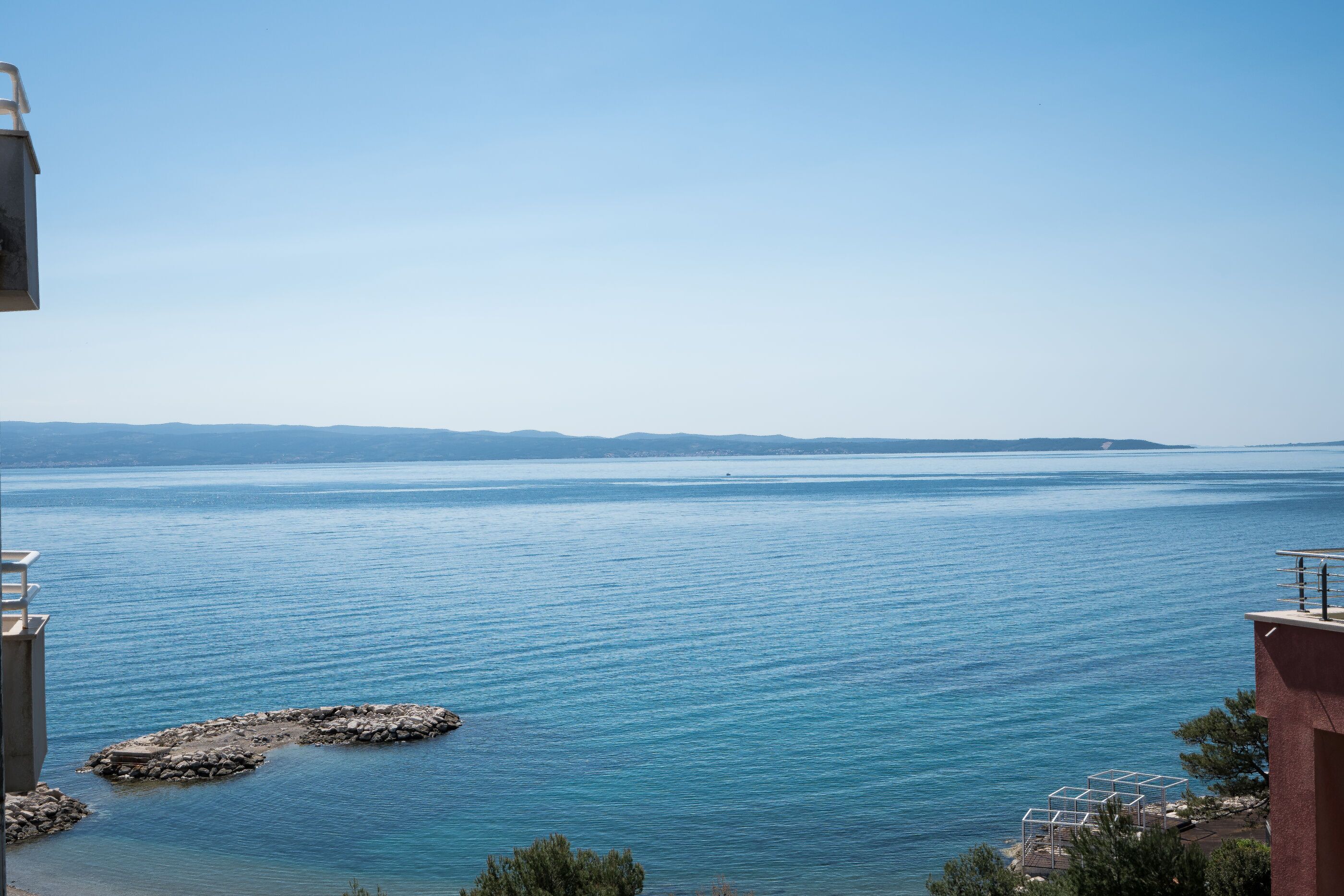 A coastal view with a clear sky, calm sea, and rocky outcrops.