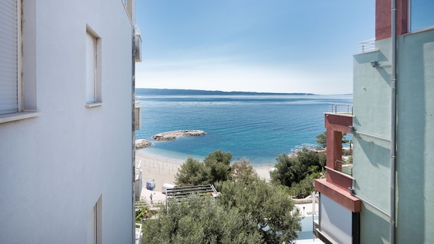Vista costera desde un edificio con balcón que da al mar, afloramientos rocosos y una playa.