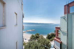 A coastal view from a building with a balcony overlooking the sea, rocky outcrops, and a beach.