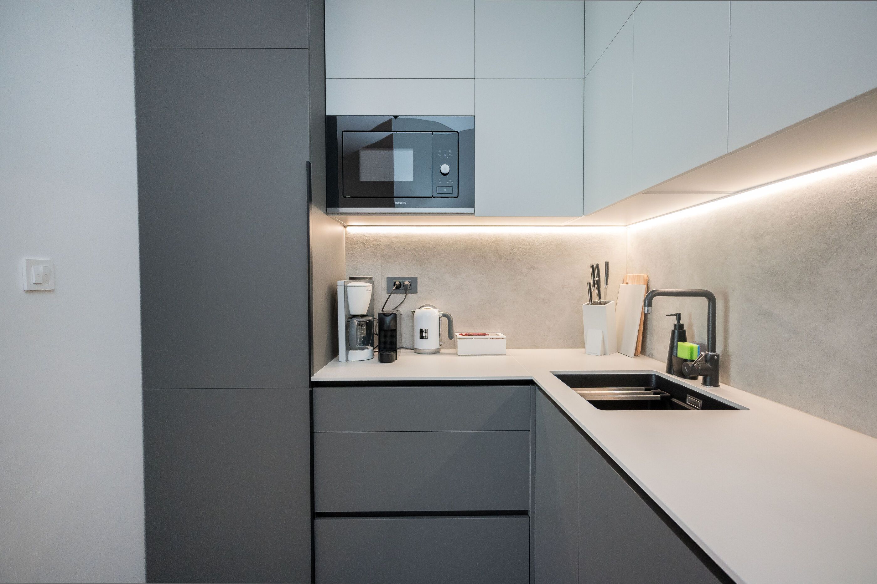 A modern kitchen with a built-in microwave, a coffee maker, a kettle, and a sink.