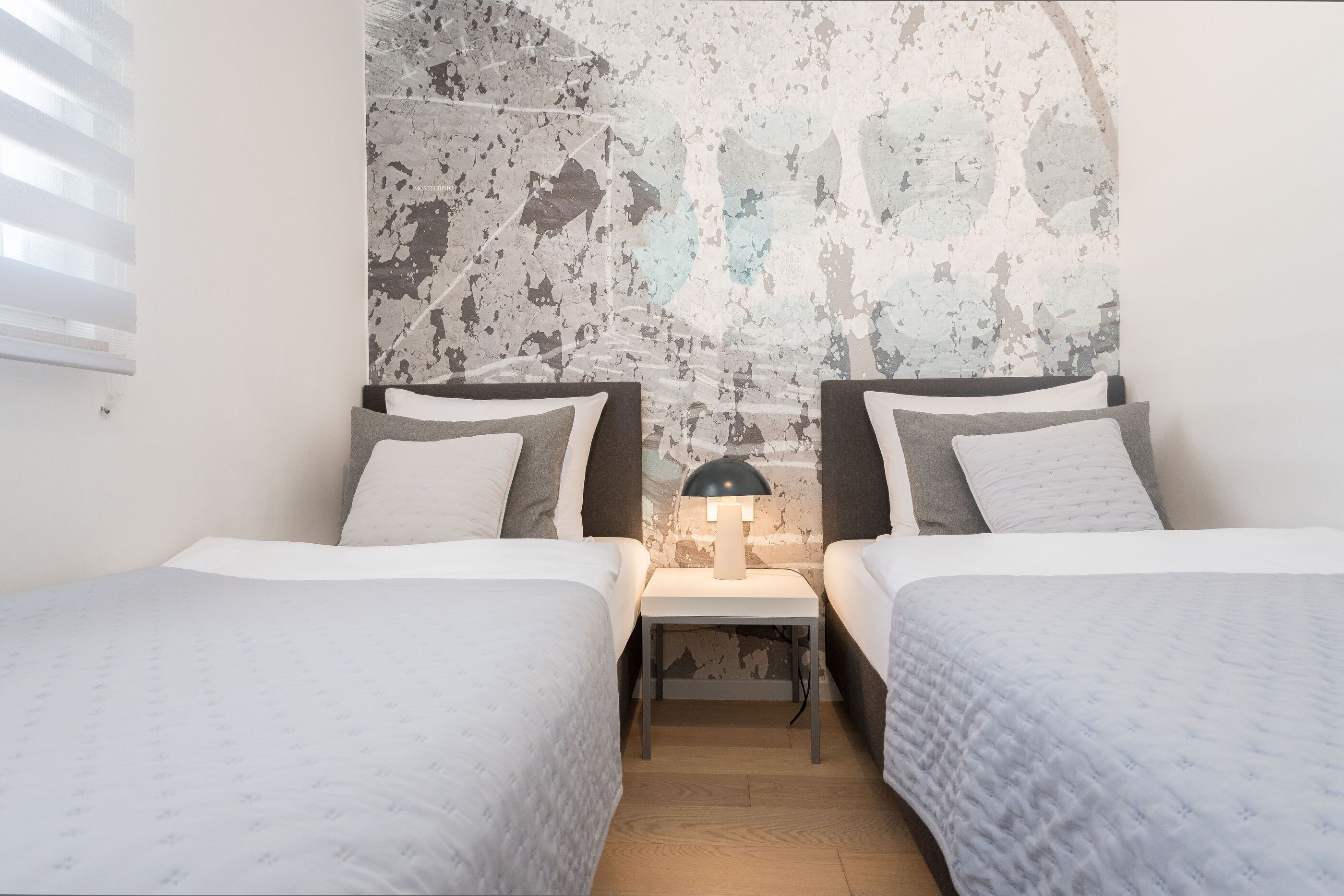 Een kamer met twee bedden, een nachtkastje met een lamp en een structuurwand.