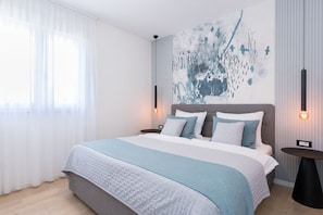 Quarto de hotel moderno com uma cama grande, uma obra de arte na parede e uma mesa de cabeceira com abajur.