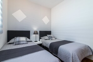 Two single beds with dark headboards and light-colored mattresses, each with a dark blanket and pillow, are positioned in this stylish room.