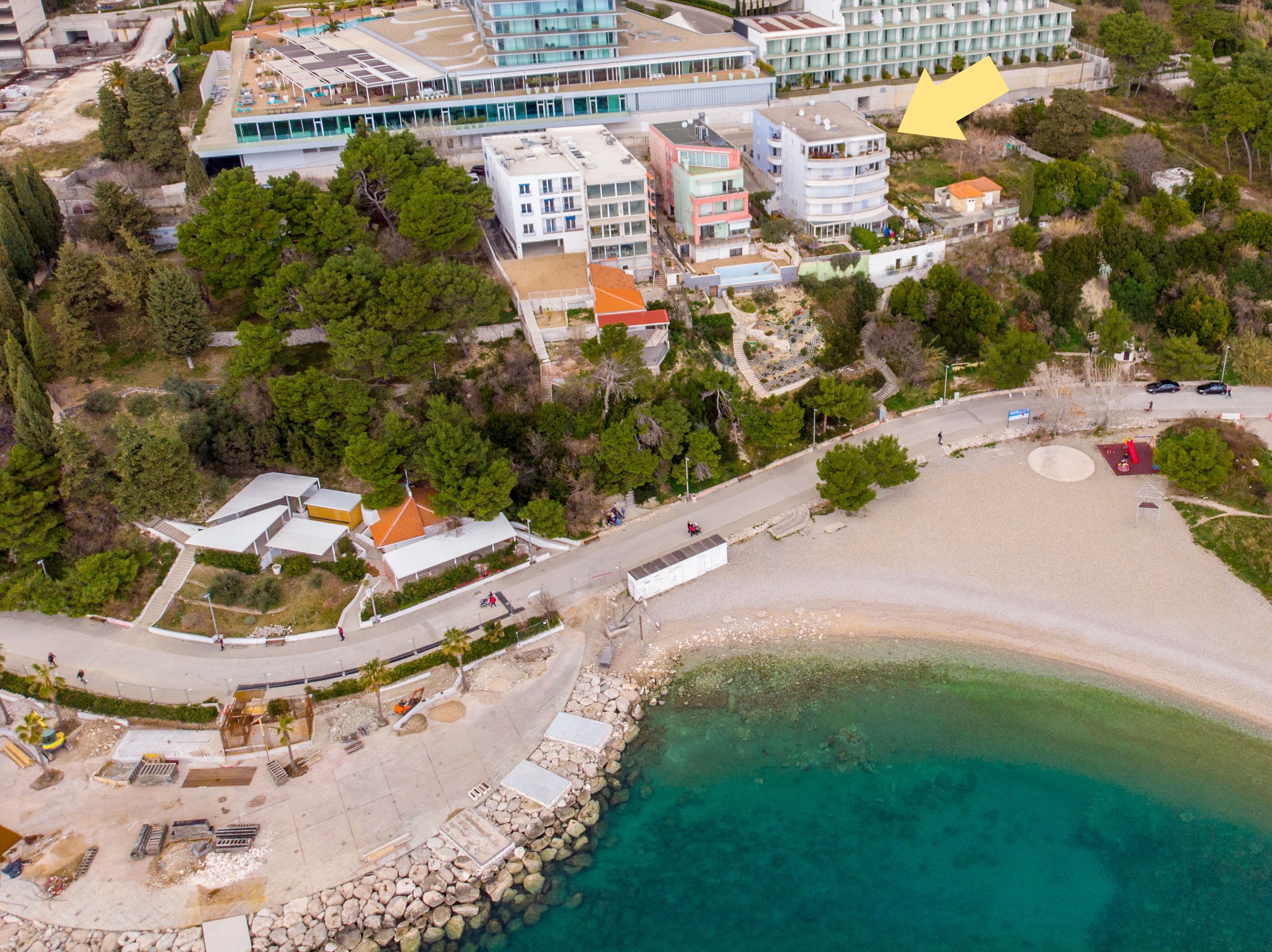 An aerial view of a coastal area with a beach, buildings, and a clear blue sea.