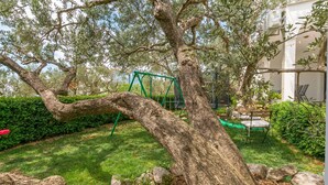 Un arbre dans un jardin, avec une balançoire fixée à ses branches.