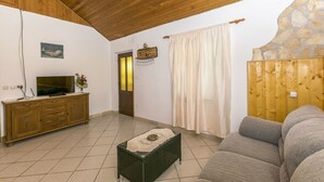 A living room with a wooden ceiling, a television on a wooden cabinet, a stone wall, and a beige curtain. - House Santa Barbara (Postira)