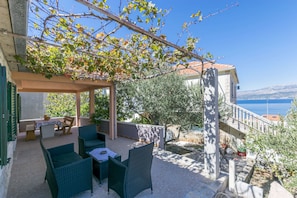A covered patio with wicker furniture, a table, and a view of the sea. - House Santa Barbara (Postira)