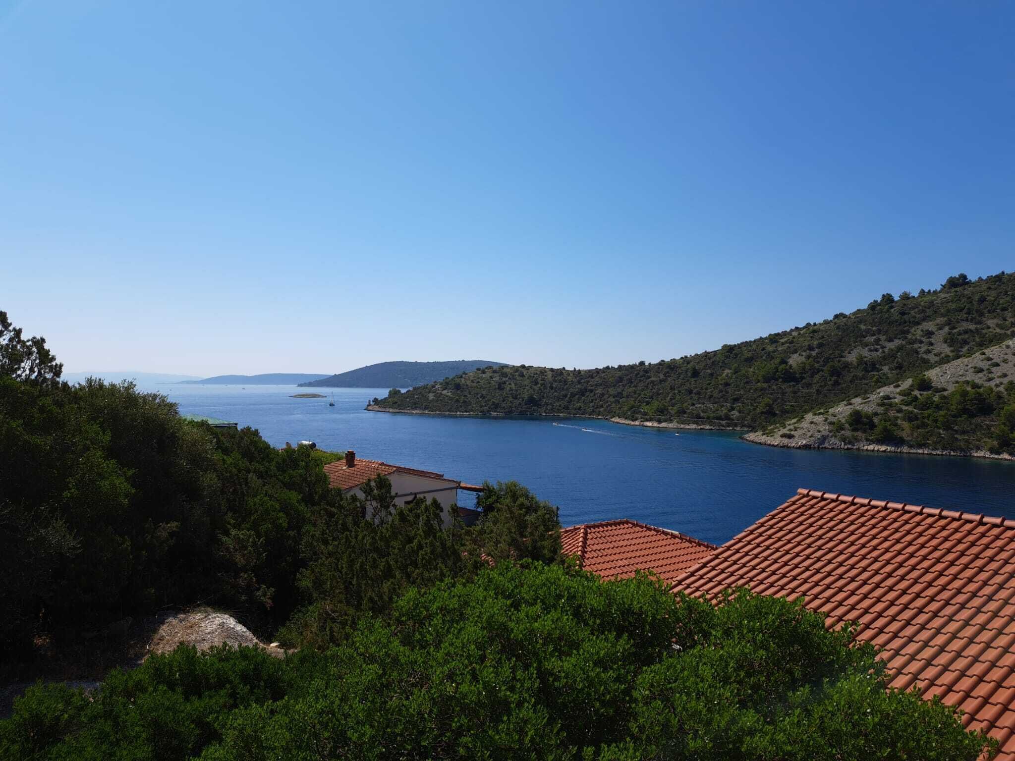 Une vue sur la côte, avec une mer bleue et limpide, des bâtiments aux toits de tuiles rouges et des collines verdoyantes.