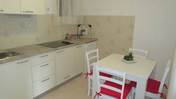 A small kitchen with white cabinets, a sink, and a dining table with four white chairs with red cushions.