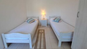 Ein kleines, sauberes Zimmer mit zwei Einzelbetten, einem Nachttisch mit Lampe und einem Kleiderschrank.
