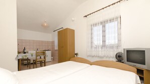 A bedroom with a bed, a TV, a wooden wardrobe, a small table with chairs, and a window with curtains. - Apartments Mirko (Okrug Gornji)