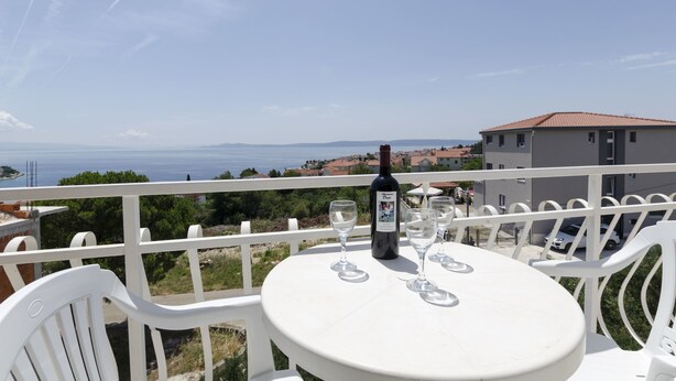 A table with a bottle and glasses on a balcony overlooking a coastal view. - Apartments Mirko (Okrug Gornji)