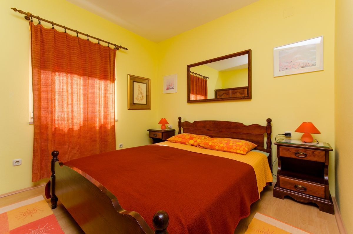 Un dormitorio con una cama grande, cabecera de madera, dos mesitas de noche con lámparas, un espejo y una ventana con cortinas.